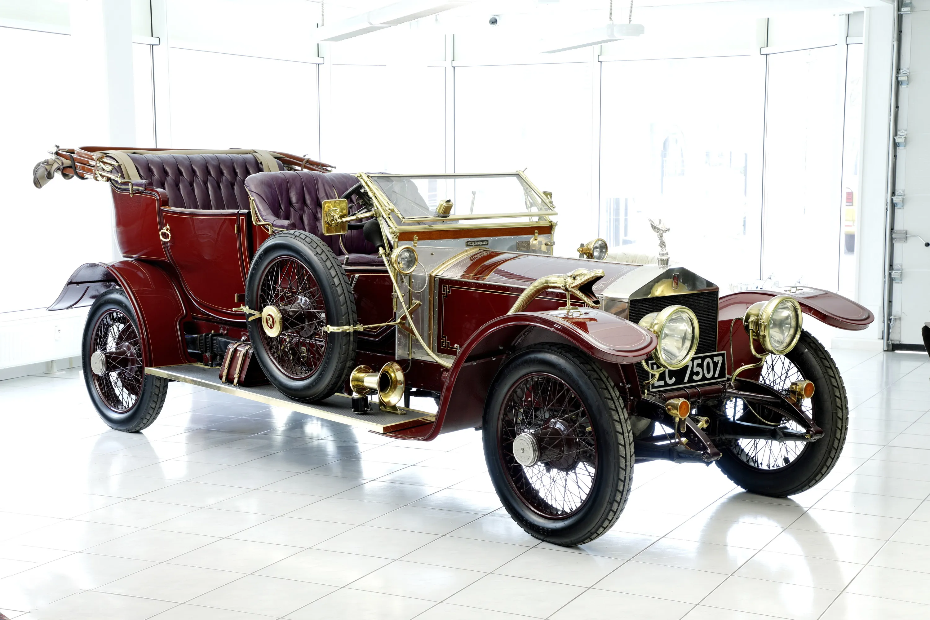 The 1913 Rolls-Royce Silver Ghost, nicknamed 'THE DUCHESS' – dark red with brass fittings and wire-spoke wheels, photographed from the front three-quarter angle in a bright showroom.