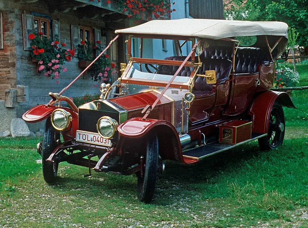 27NA photographed outside a Bavarian farmhouse in the 1980s, freshly restored in deep red livery with a Bavarian registration plate, brass fittings and a cream folding hood.